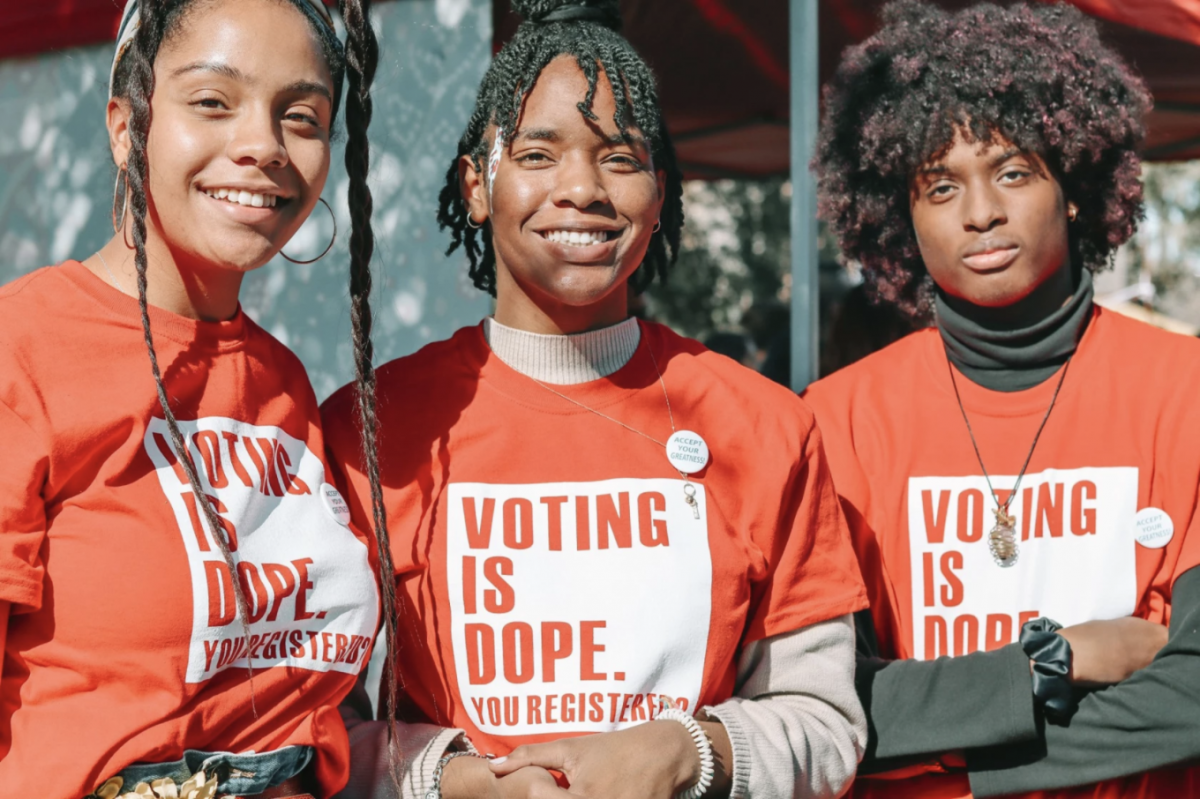 Three youth-vote organizers with Arizona Coalition for Change stand together wearing orange t-shirts that say, 