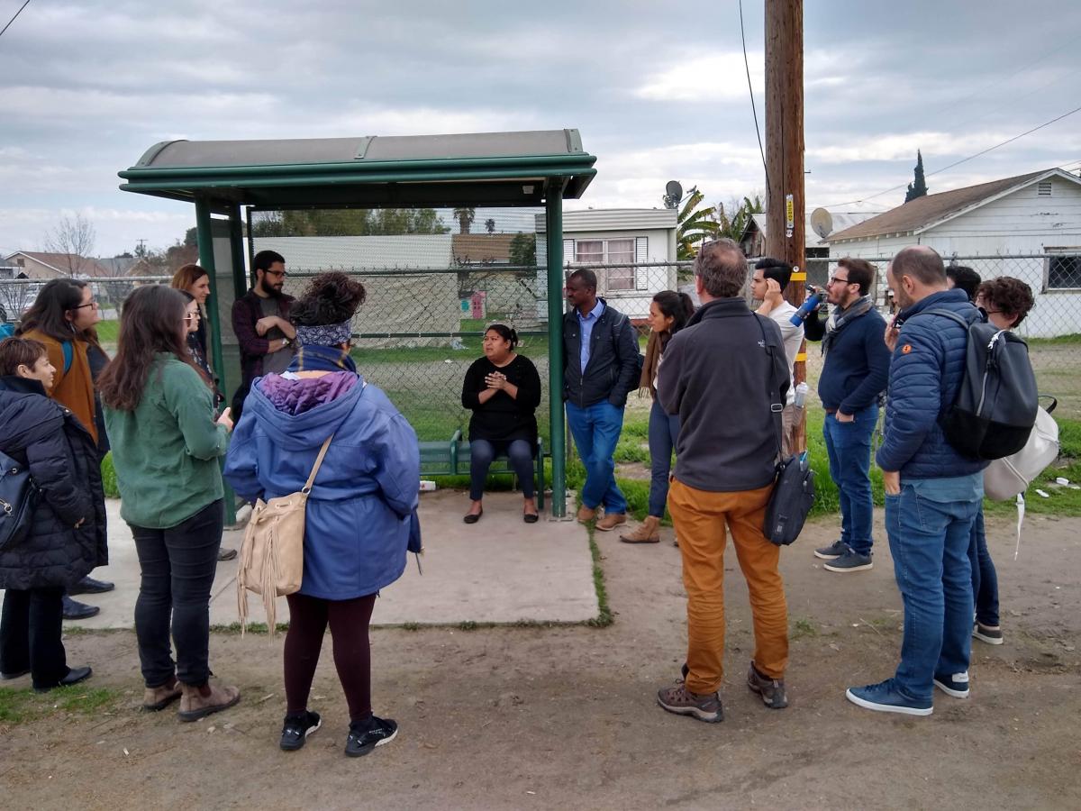 Isabel speaking to a group in front of a neighborhood bus stop.