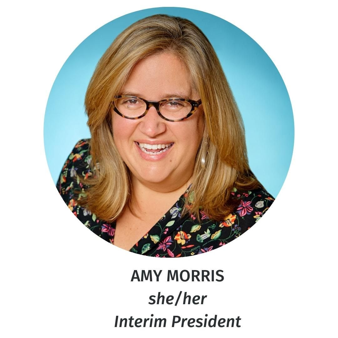 Amy Morris smiling while wearing glasses and a black floral top.