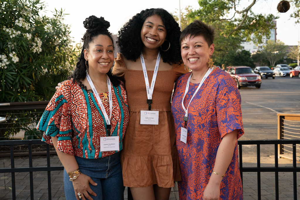 A photo of the NFG Membership and Communications Team. Pictured left to right: Lauren Goudeaux in a coral and green short sleeved blouse and jeans, Hallie McClain in an orange dress, and Courtney Banayad in a hot pink and purple short sleeved dress.