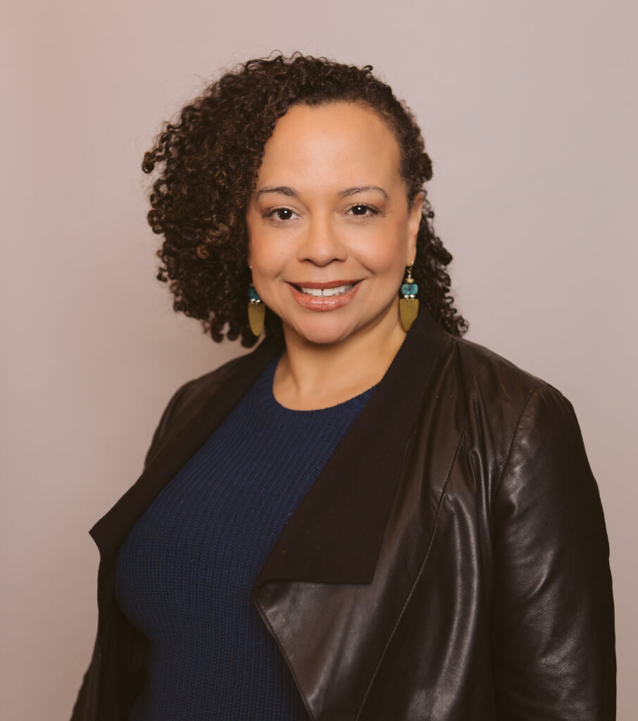 Headshot for Leticia Peguero. Leticia wears a dangly earrings, a navy sweater, and a black jacket.