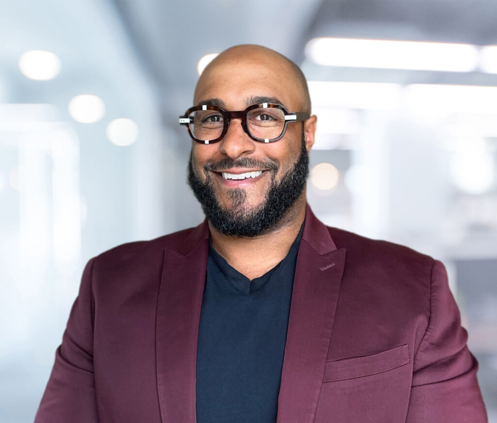 Headshot for Andrew Plumley. Andrew wears brown tortoise shell with white accents, a maroon blazer, and a black shirt.