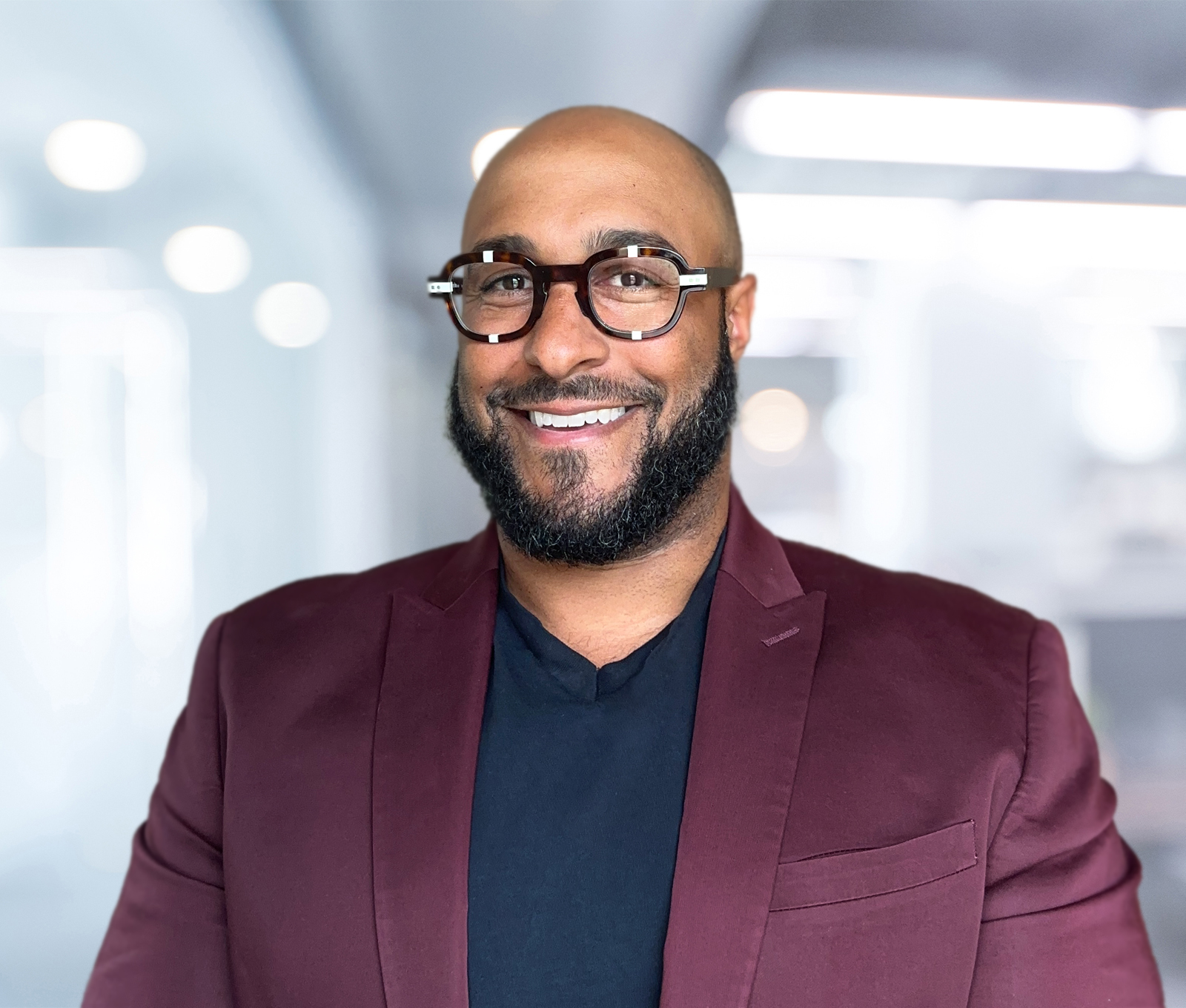 Headshot for Andrew Plumley. Andrew wears brown tortoise shell with white accents, a maroon blazer, and a black shirt.
